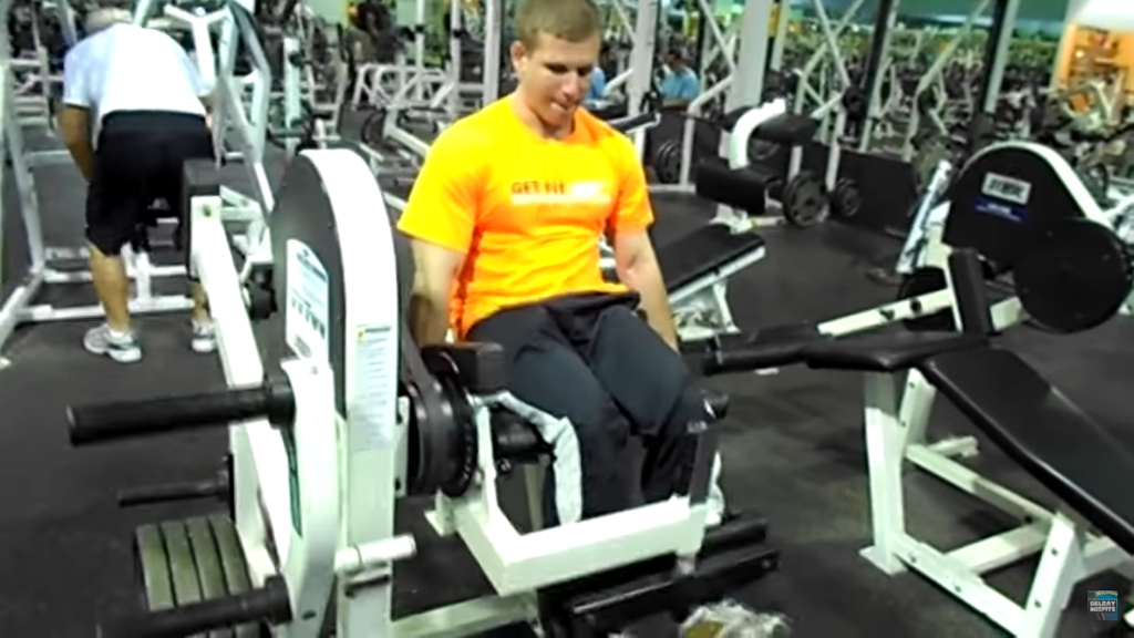 man in a yellow t-shirt using a leg press machine at a fitness center