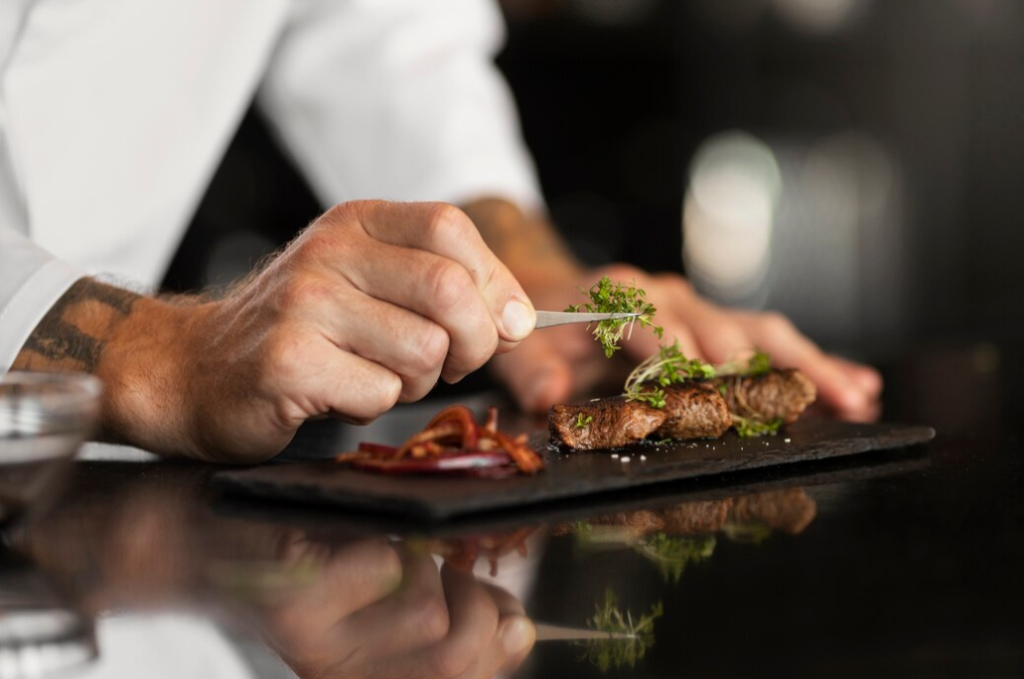 Chef precisely garnishing a steak with herbs on a black slate plate