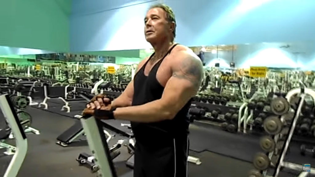 Man in gym resting on equipment surrounded by weights