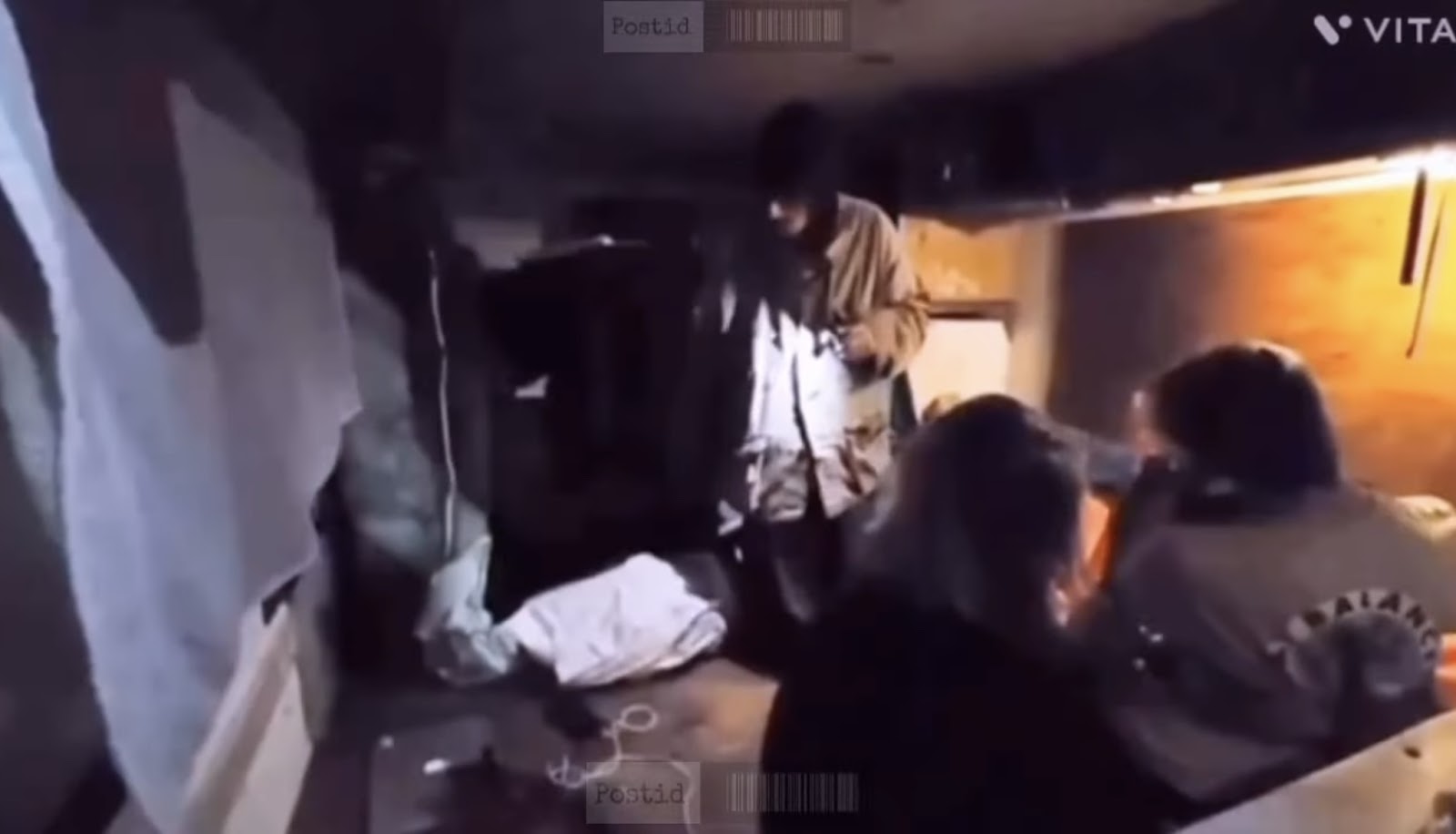 Cluttered room with three individuals. The room has a sense of disarray, with various items strewn around
